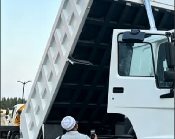 Customer inspects refurbished HOWO 371HP 6×4 dump truck with raised cargo box at factory yard